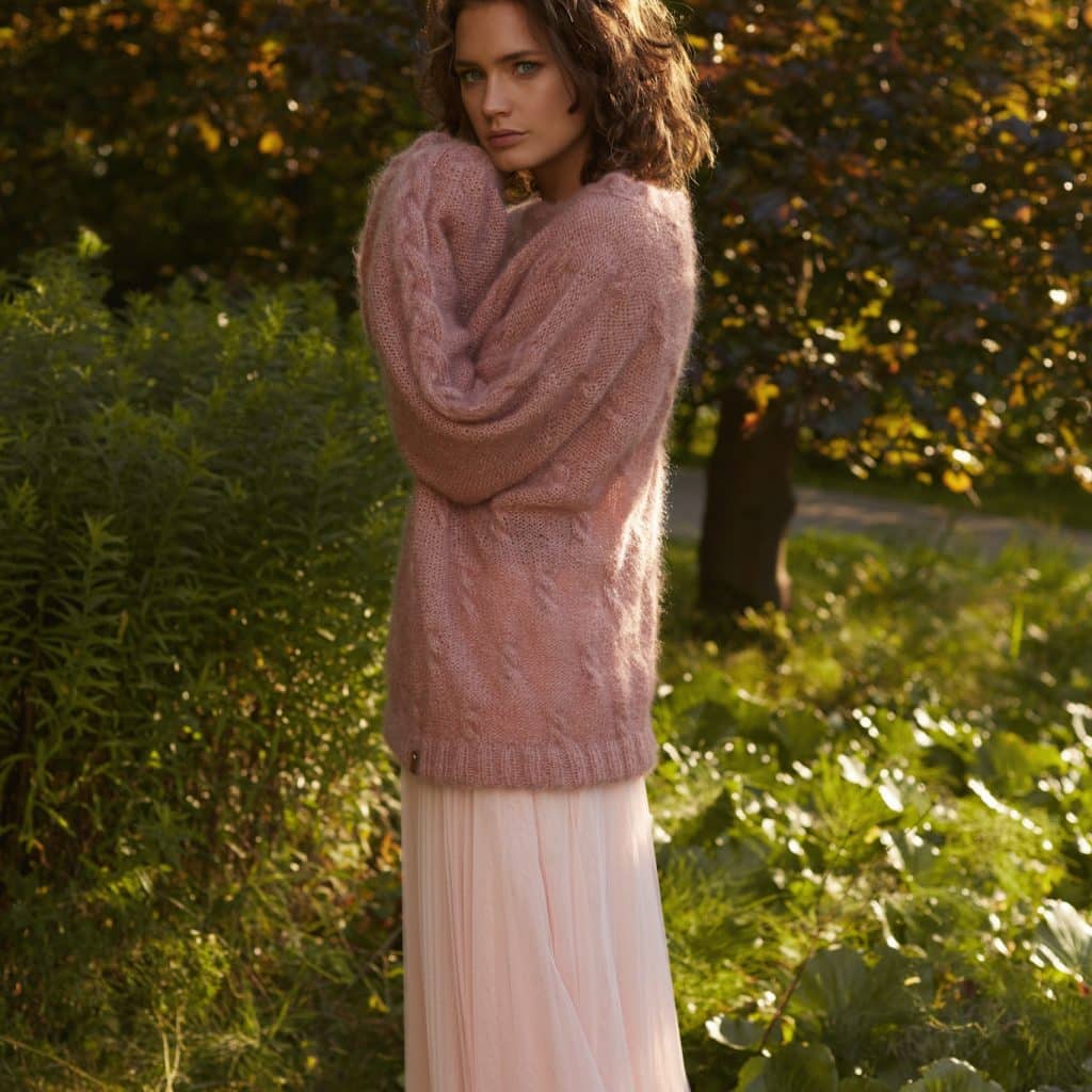 Sweter z moheru różowy oversize ręcznie robiony Element no 2 zestawiony ze zwiewną pastelową spódnicą na tle zieleni.