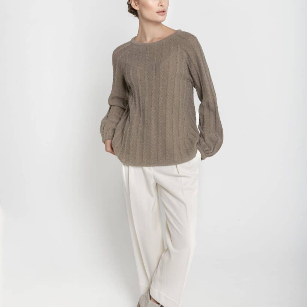 Ręcznie robiony na drutach sweter z merynosa i kaszmiru ESSENTIAL No 1 taupe z bufiastymi rękawami - widok z przodu na modelce. Zestawiony z białymi spodniami i szarymi botkami.